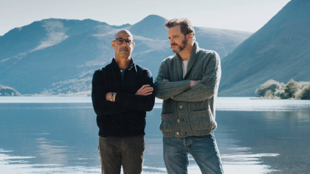 Two men stand next to each other with their arms crossed, with the blue water and the blue mountains behind them.